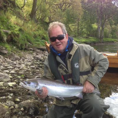 This salmon fisher is holding a perfect late Spring salmon that we caught from the boat on the River Tay. You can see the fishing guest's life jacket and waterproof clothing that our salmon fishing guides supply all salmon fishing trip guests. You can also see the beautiful traditional River Tay salmon fishing boat in the back ground which often provides a fishing advantage.