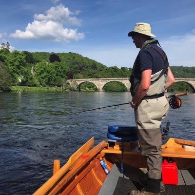 Here's a salmon fly fisher out in a traditional River Tay coble boat covering the Cathedral Stream salmon pool with a fly rod. This is a great area for a resting salmon to be located that's navigated up through the fast water below the bridge. The Telford Bridge you can see in the shot is over 200 years old and joins the village of Birnam to the town of Dunkeld.