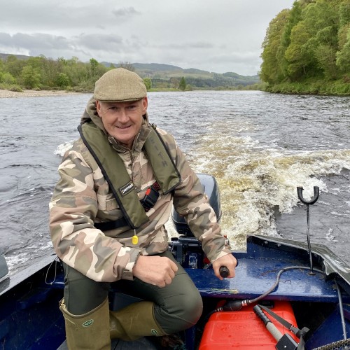Here's Jock Monteith powering upstream in a traditional larch built River Tay salmon fishing 'coble' boat at the confluence of the River Tay & River Tummel during the month of May. Jock has his cold weather clothing on and Tweed cap in addition to his life jacket which is essential for all boat or riverbank duties.
